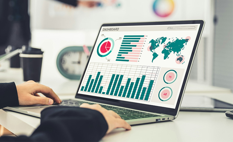 A professional workspace showing a laptop displaying various colorful business growth charts and data analytics, with a person's hands nearby on a desk. The image conveys a sense of B2B digital strategy and local SEO performance tracking.