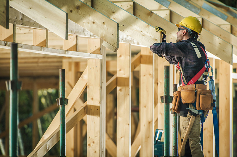 A construction professional in a safety vest and hard hat stands on a high-level scaffolding overlooking a residential building project. He is looking out over the site, representing the hands-on expertise and oversight involved in Twin Cities contracting and construction management.